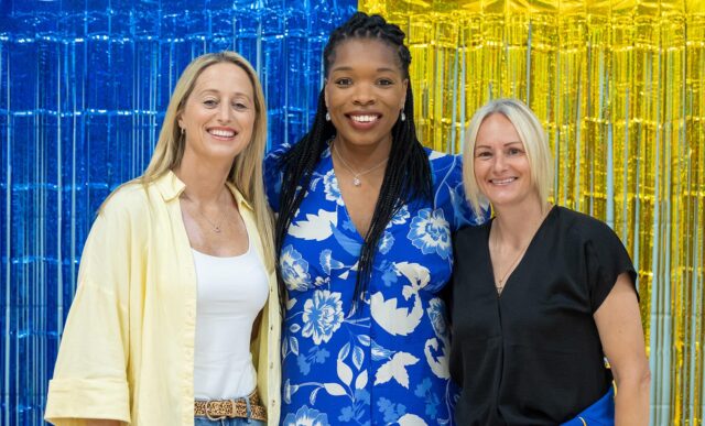 Jess Thirlby, Eboni Usoro-Brown and Clare Elsley stood in front of blue and gold ribbons at Team Bath.