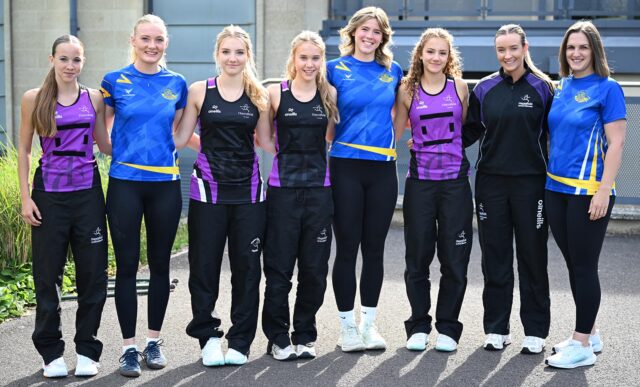 Team Bath Netball players and staff, wearing blue tops, with pupils and staff from Hayesfield Girls School, wearing purple and black tops.